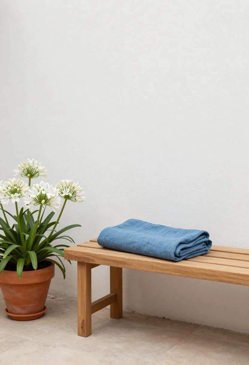 Teak bench with a steel blue throw against a whitewashed garden wall in soft morning light